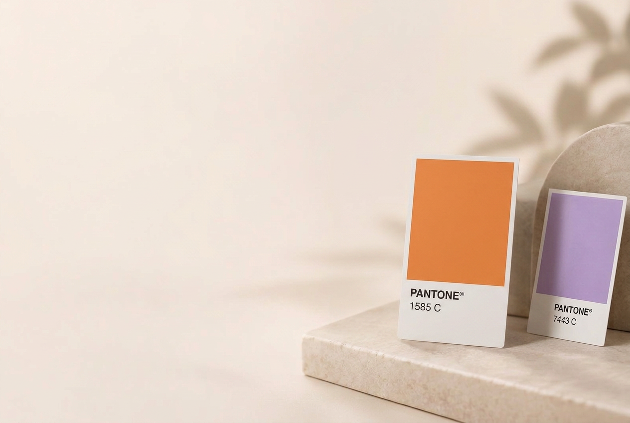 Two Pantone colour swatch cards, one warm orange and one soft lavender, resting on a pale stone pedestal beside a curved stone arch